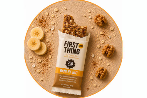 A wrapped Banana Nut bar photographed from above with a bite taken out of the top, framed in a gold circle, with banana slices, walnuts and oats around it