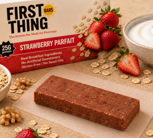 One unwrapped Strawberry Parfait bar on parchment in front of a Strawberry Parfait box, with fresh strawberries and a bowl of yogurt