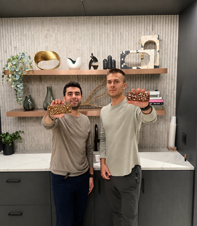 Christian Mancheno and Ben Fuhrmann standing in a kitchen, each holding up a First Thing bar