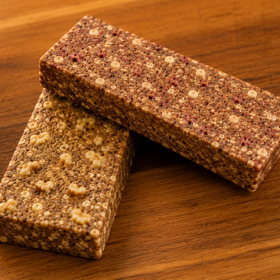 Two First Thing bars resting on each other on a wood table, close enough to see the oats, puffed grains and fruit pieces pressed through them