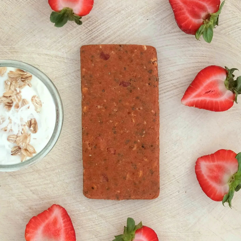 A Strawberry Parfait bar seen from above on a pale wood table, ringed by halved strawberries beside a glass of yogurt topped with oats and coconut